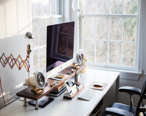 A well-organized modern office desk with a computer monitor, plants, and natural light